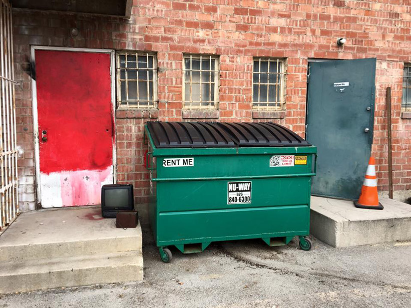 A photo of a dumpster behind a building.