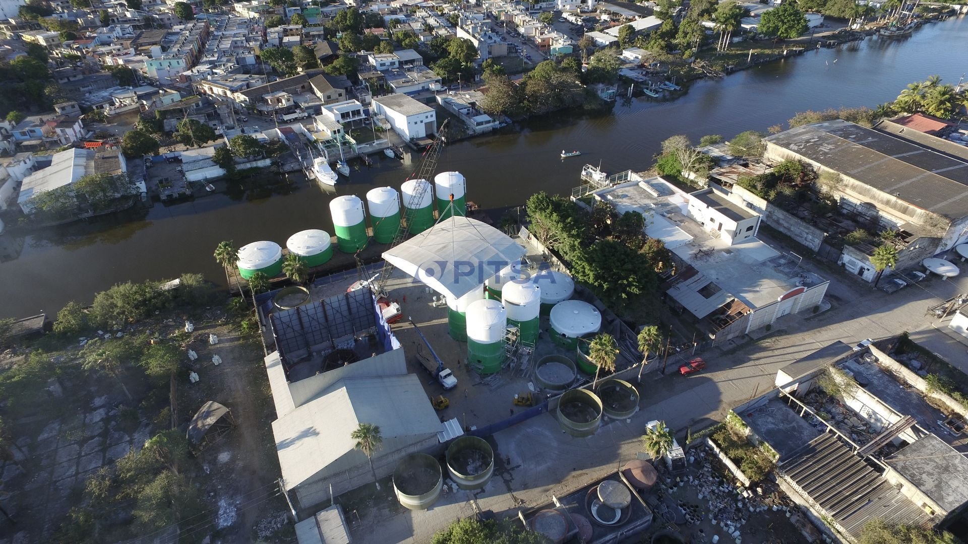 Aerial view of large green and white FRP tanks at PITSA's waterfront facility, ready for maritime transport, surrounded by industrial buildings.