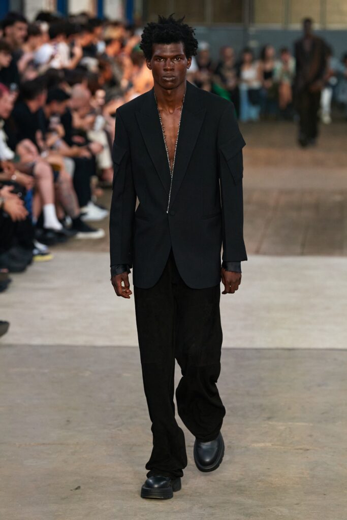 A relaxed black blazer with a V-neck and asymmetric design paired with matching pants.