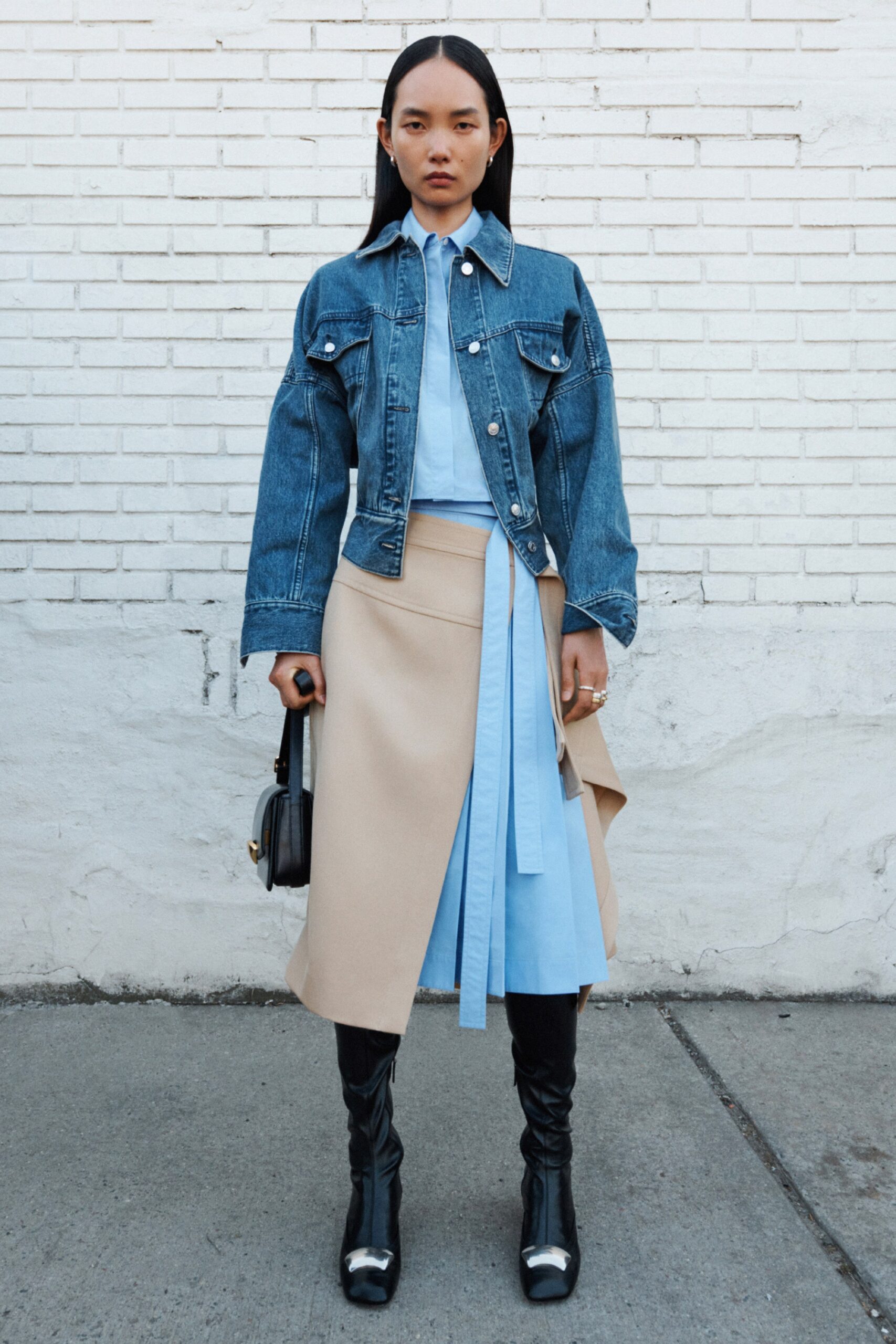 A fitted blue denim jacket paired with an asymmetric beige skirt, featuring layered details.