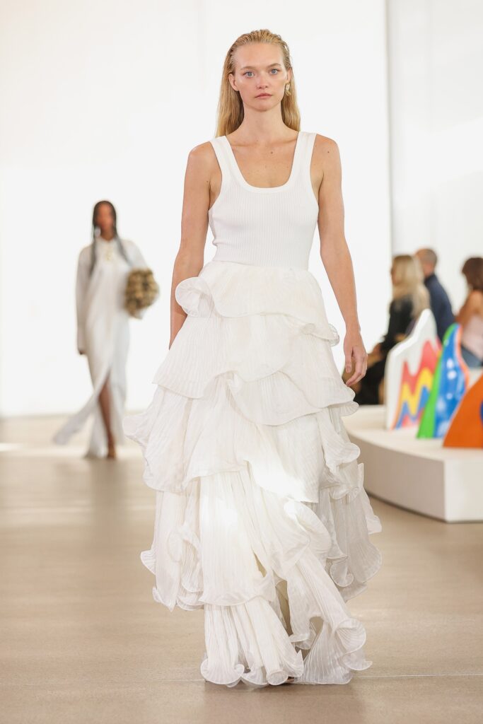 A fitted white sleeveless dress with a high neckline and tiered design.