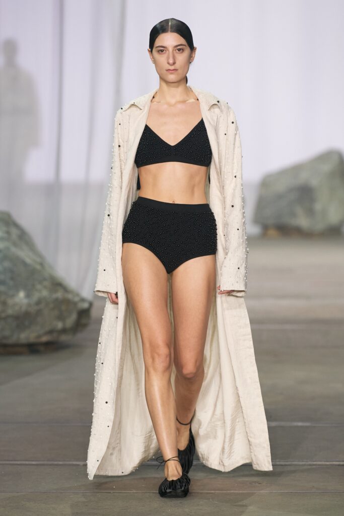 A fitted white coat layered over a black bikini, featuring a sleeveless design.