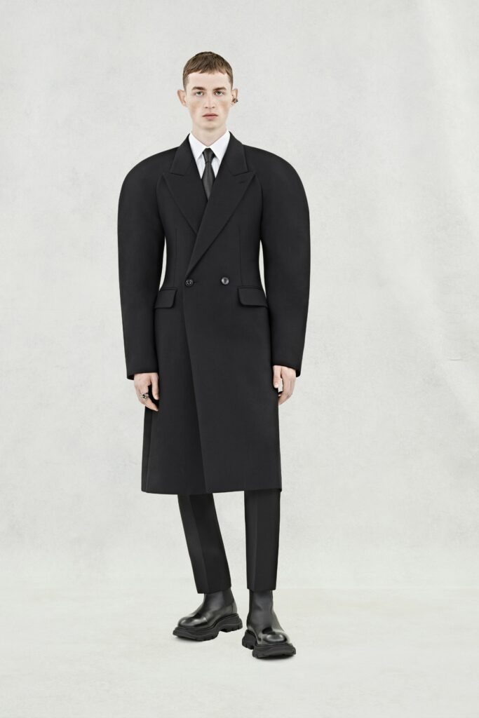 A structured black wool coat with long sleeves and a double-breasted design, paired with tailored pants.