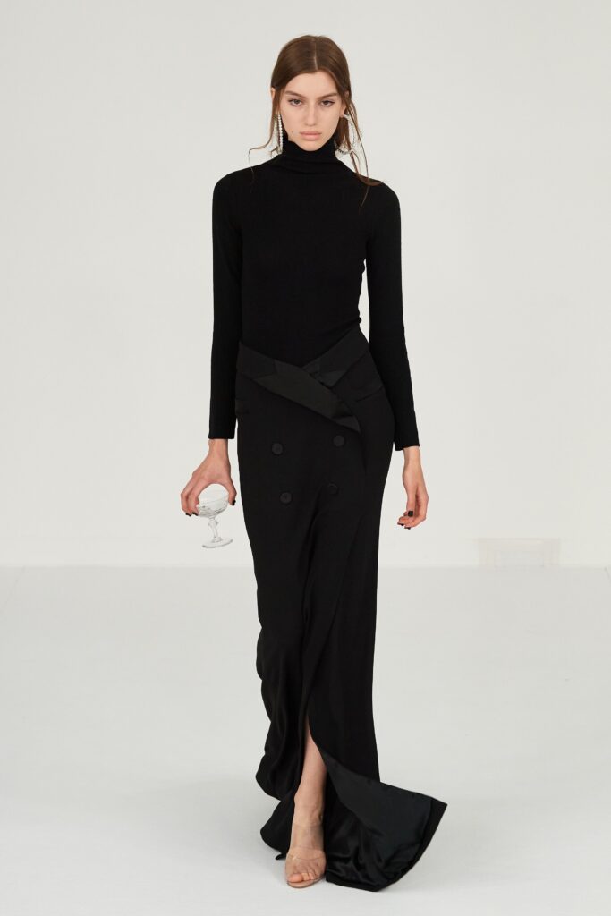 A fitted black silk dress with long sleeves, a high neckline, and a stylish slit.