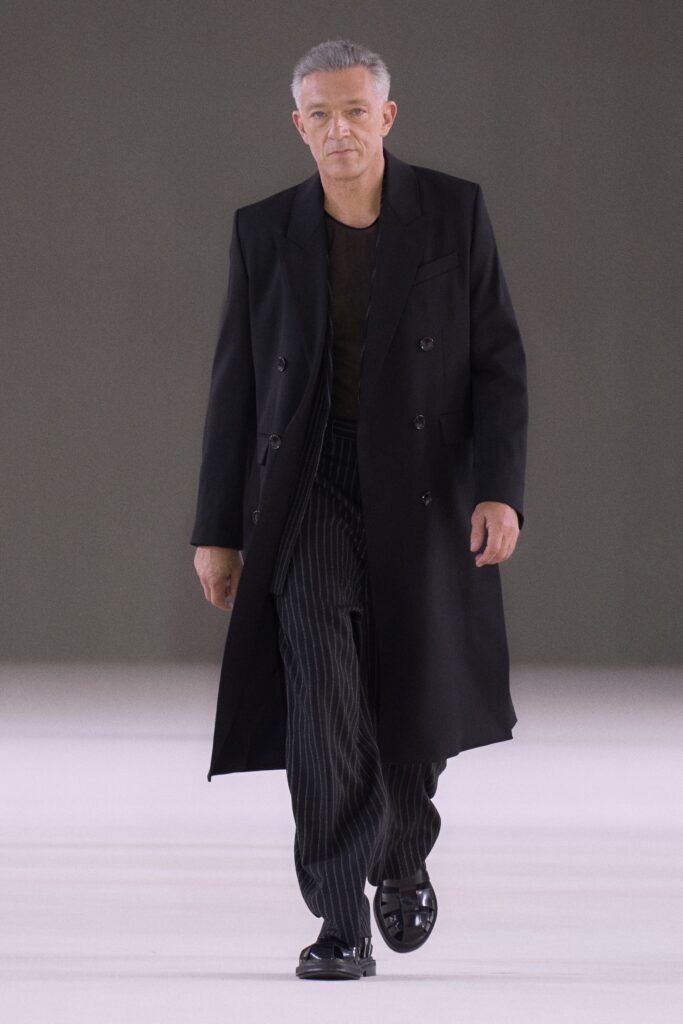 A relaxed black wool coat with a collared design paired with striped pants.