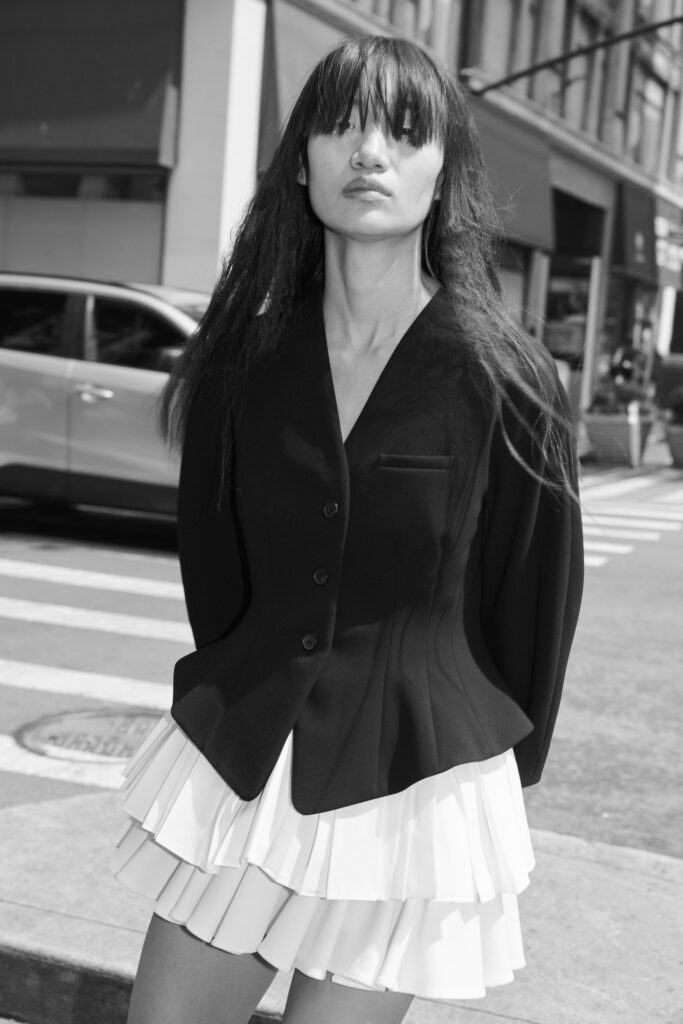 A fitted black jacket over a pleated white dress with an asymmetric design.