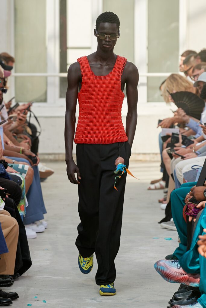 A fitted sleeveless red pleated top paired with black pants, showcasing a modern silhouette.