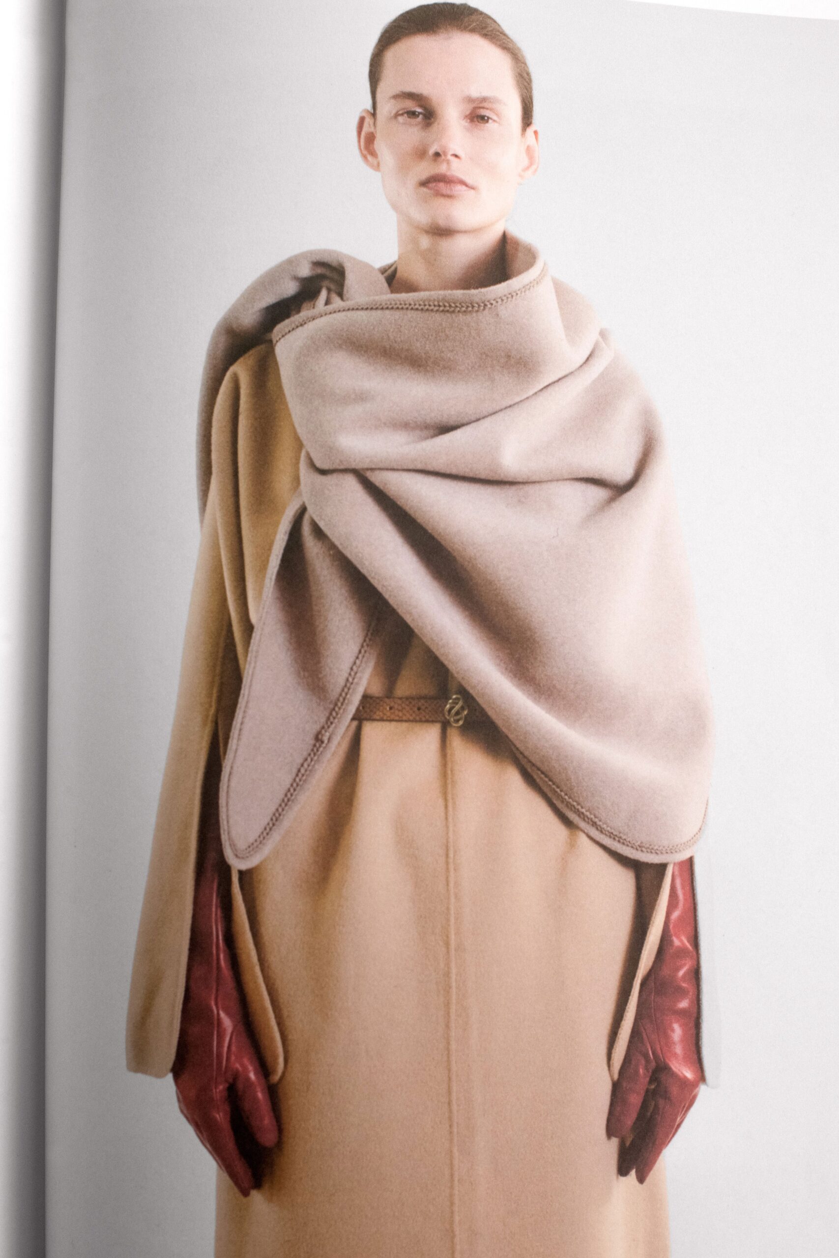A relaxed beige wool coat layered with a cape and complemented by brown leather gloves.