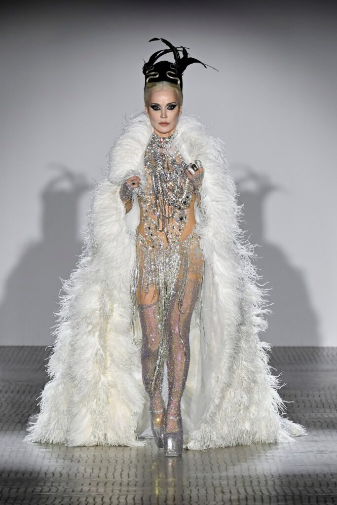 A fitted white sequined dress with a sleeveless design, layered with a dramatic fur cape.