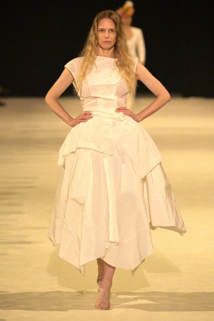 A fitted white sleeveless dress with a high neckline and tiered design.