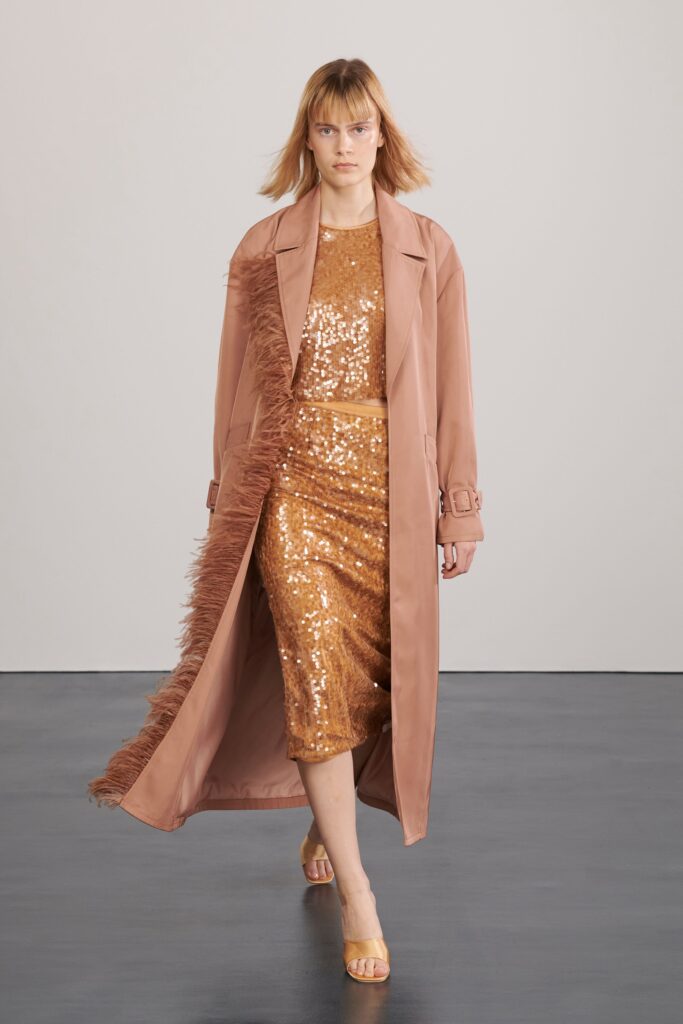 A fitted pink silk dress adorned with sequins, complemented by a long collared coat.