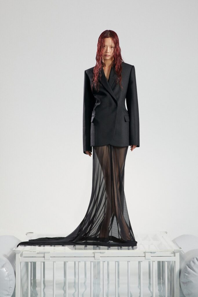 A fitted black blazer dress with a V-neckline and layered sheer details.