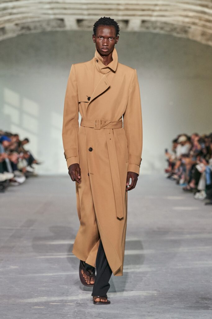 A relaxed beige cotton trench coat with long sleeves and a belted design.