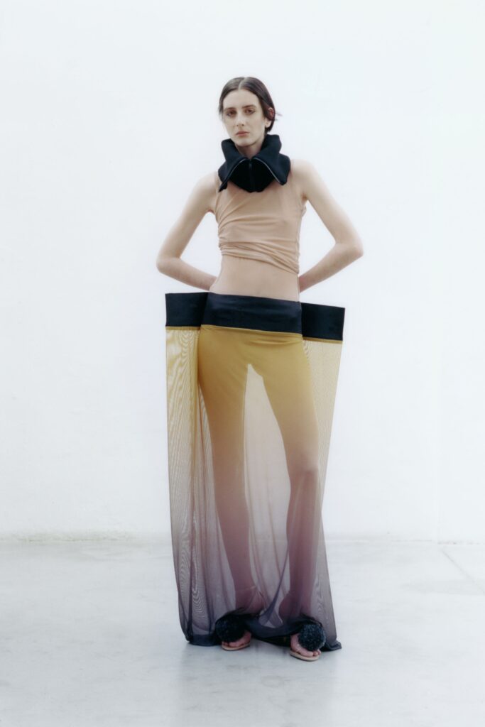 A fitted beige silk sleeveless dress with a high-neck and asymmetric design.