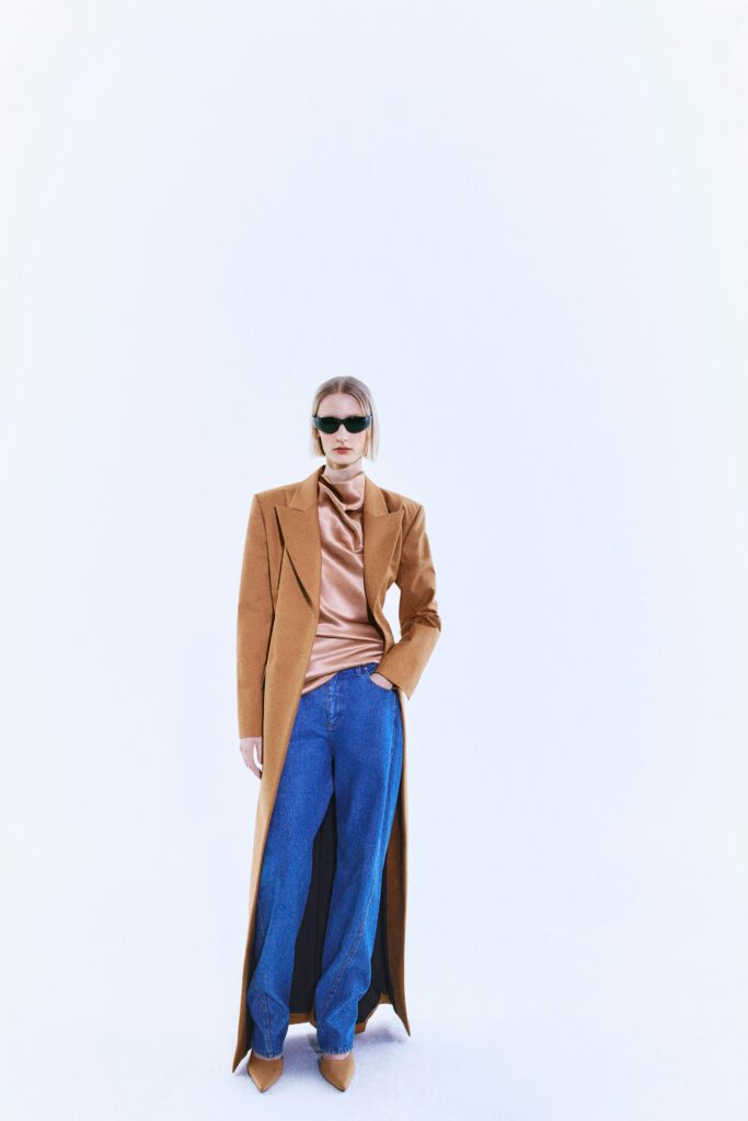 A relaxed brown coat paired with a beige top and blue wide-leg pants.