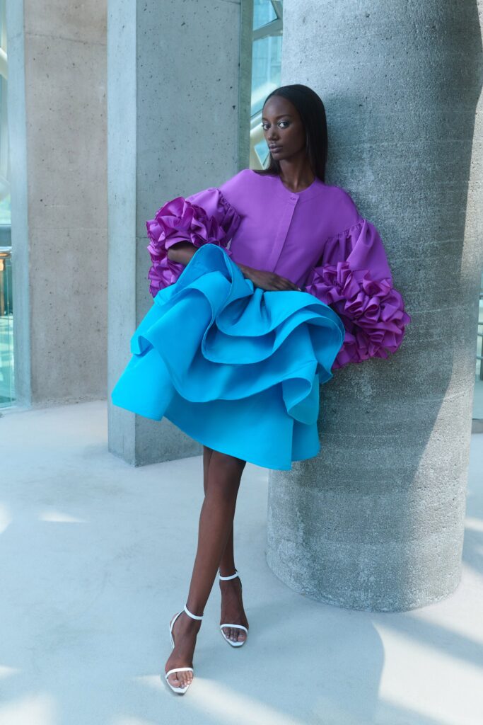 A fitted blue and purple dress with long sleeves, a collared neckline, and ruffled tiered design.