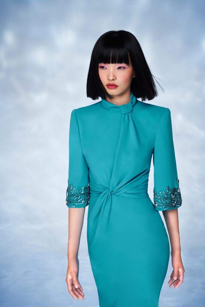A fitted blue silk dress with long sleeves and a high neckline featuring ruched detailing.