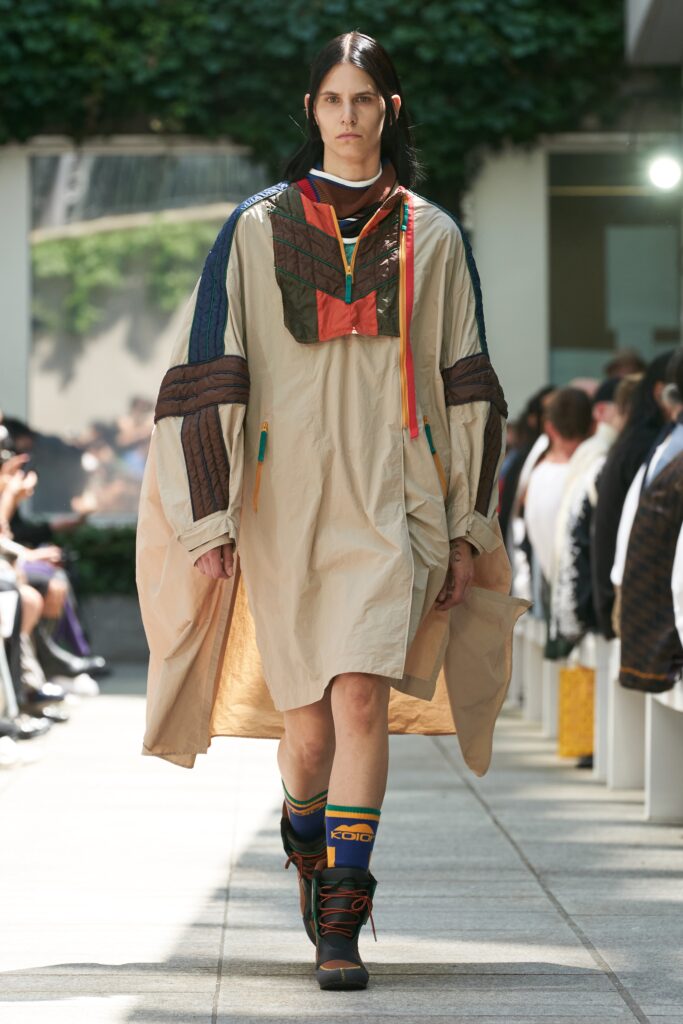 An oversized beige dress with long sleeves and a collared neckline featuring layered design details.