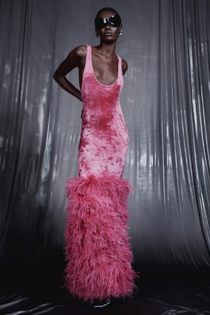 A fitted pink velvet dress with a high neckline and tiered feather detailing at the hem.