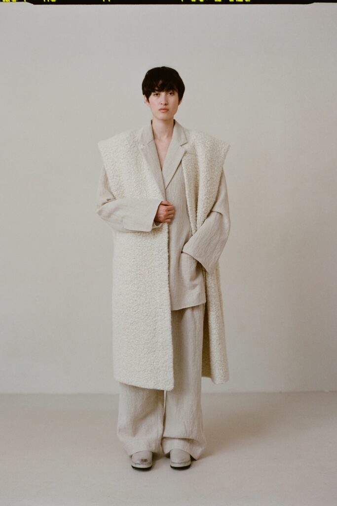 A relaxed beige wool coat paired with matching relaxed-fit pants, featuring a layered design.