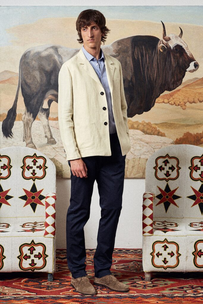 A tailored beige cotton jacket with long sleeves and a collared design, paired with navy pants.
