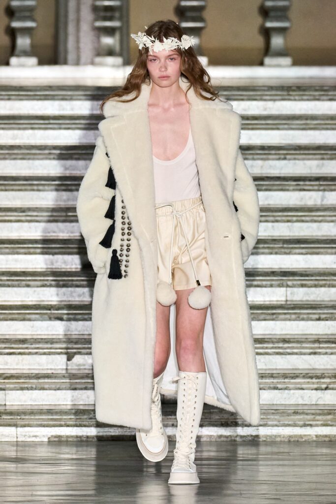 A relaxed white fur coat paired with beige silk shorts and a V-neckline.