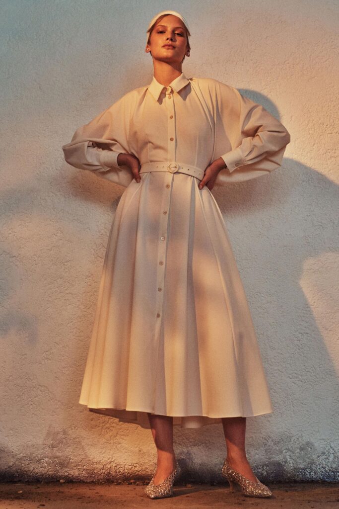 A relaxed beige dress with long sleeves, a collared neckline, and pleated design details.