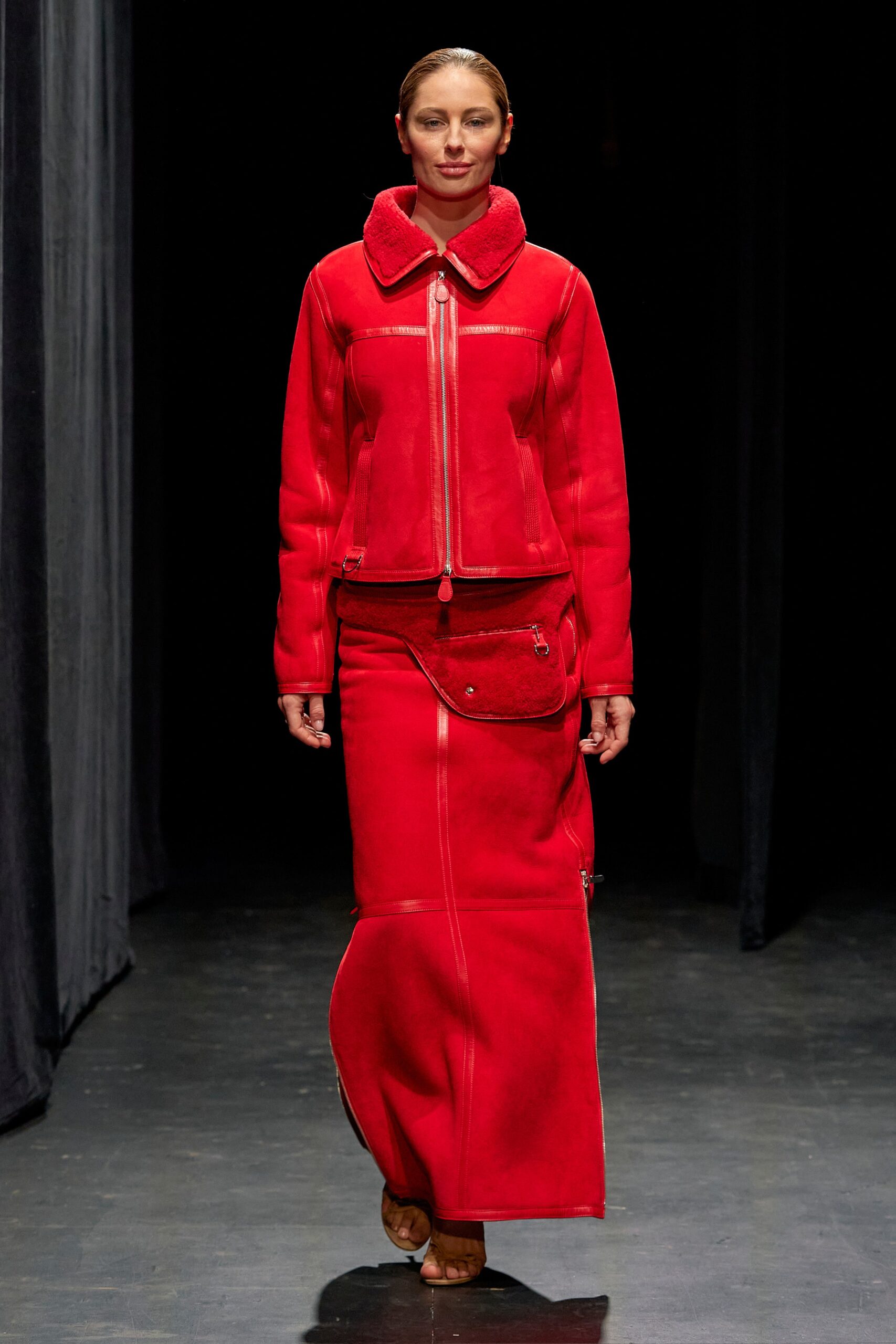 A fitted red leather jacket with a collared neckline paired with a zippered asymmetric skirt.