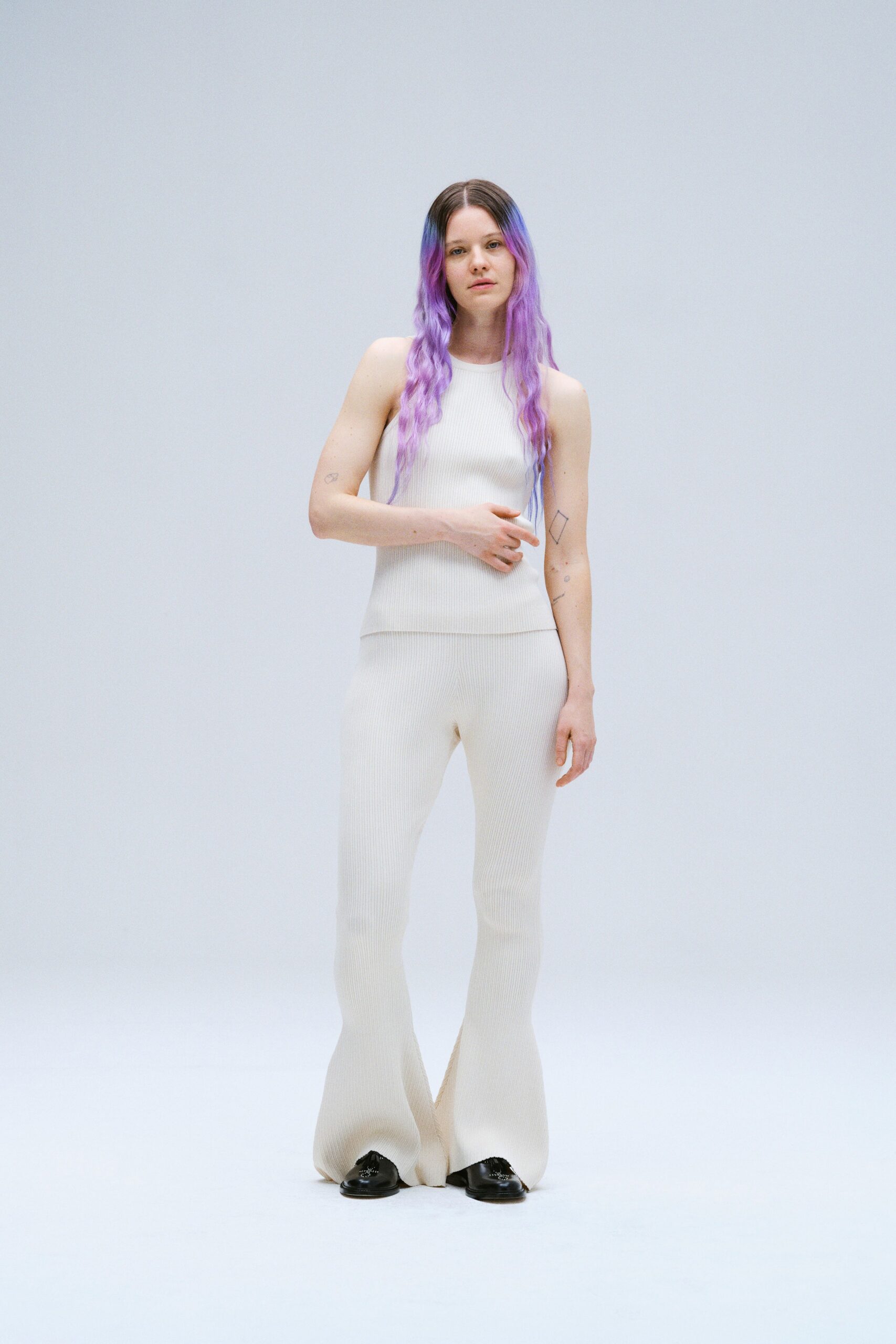 A fitted white sleeveless knit top paired with flared pants for a stylish look.