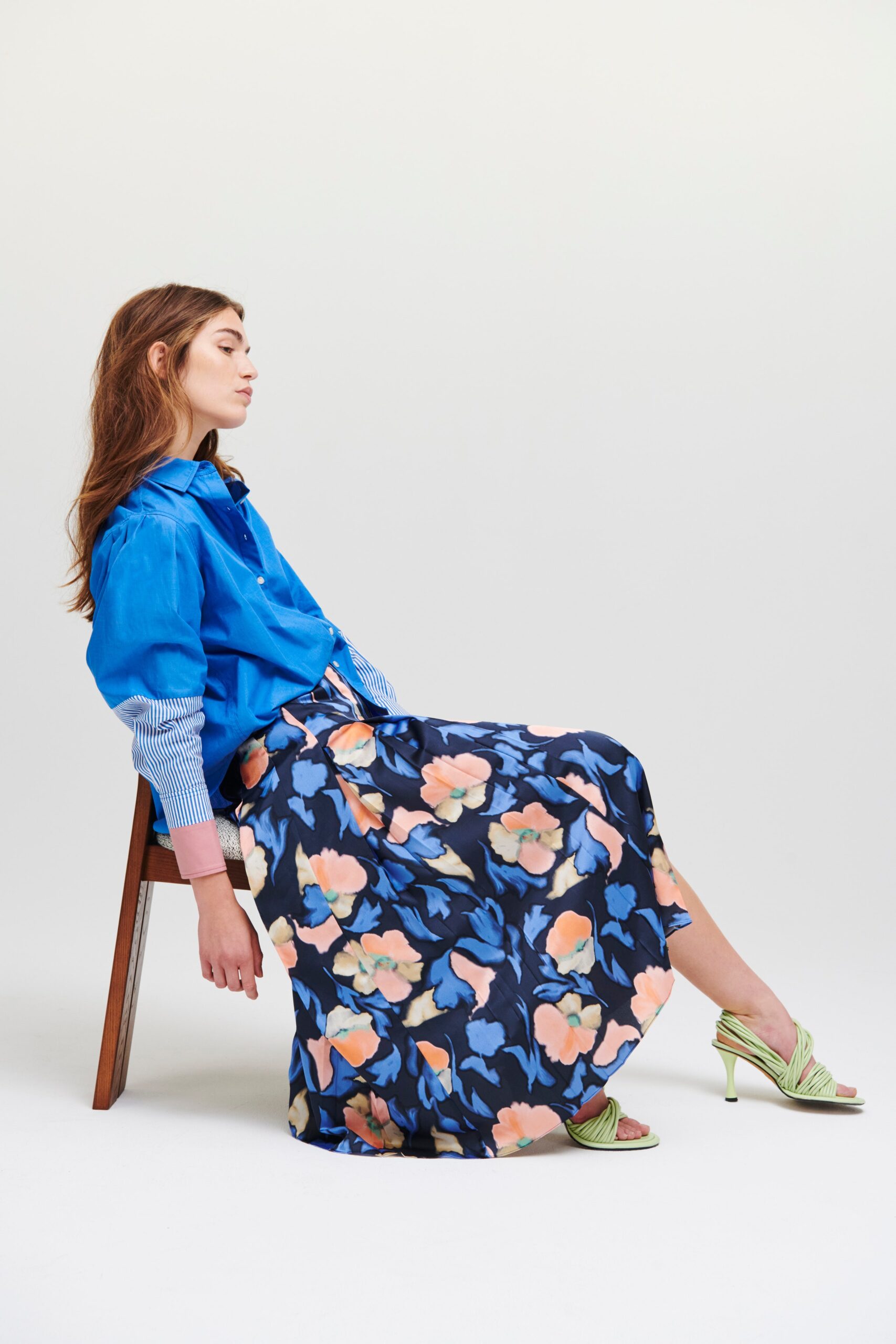 A relaxed blue cotton shirt with long sleeves paired with a multicolor flared skirt.