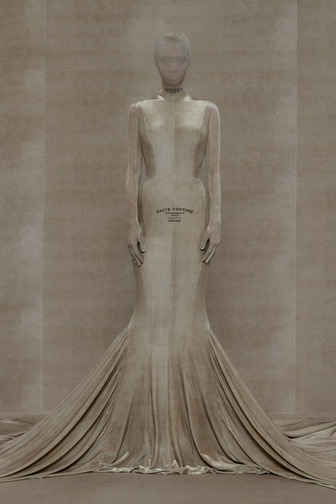 A fitted beige silk gown with long sleeves and a high neckline featuring a draped design.