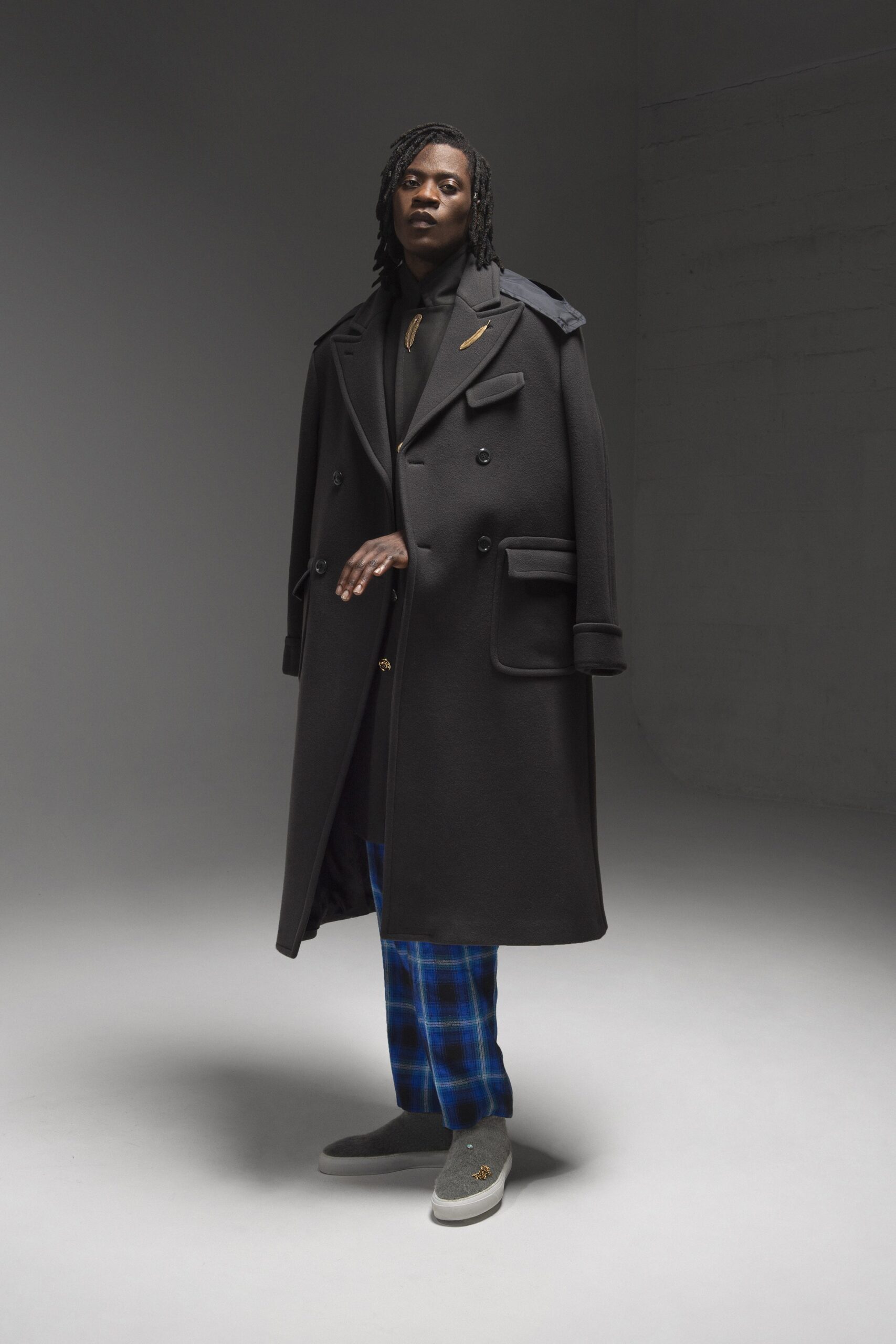 A relaxed black wool coat with long sleeves and a collared design, paired with checked blue pants.