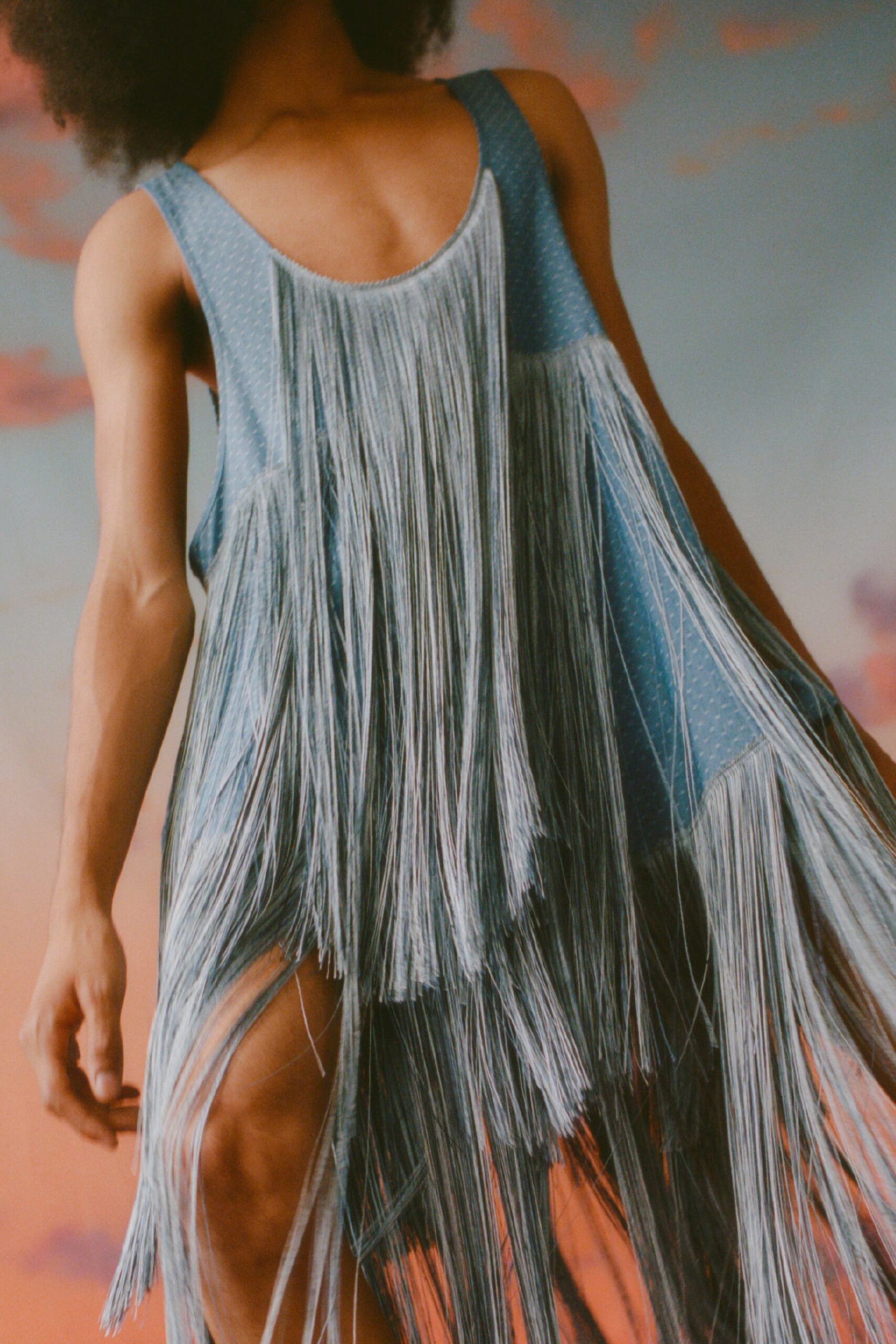 This relaxed sleeveless dress features an eye-catching high-neck design, adorned with cascading fringes that create dynamic movement. The asymmetric silhouette adds a contemporary edge, making it a striking choice for bold expression.