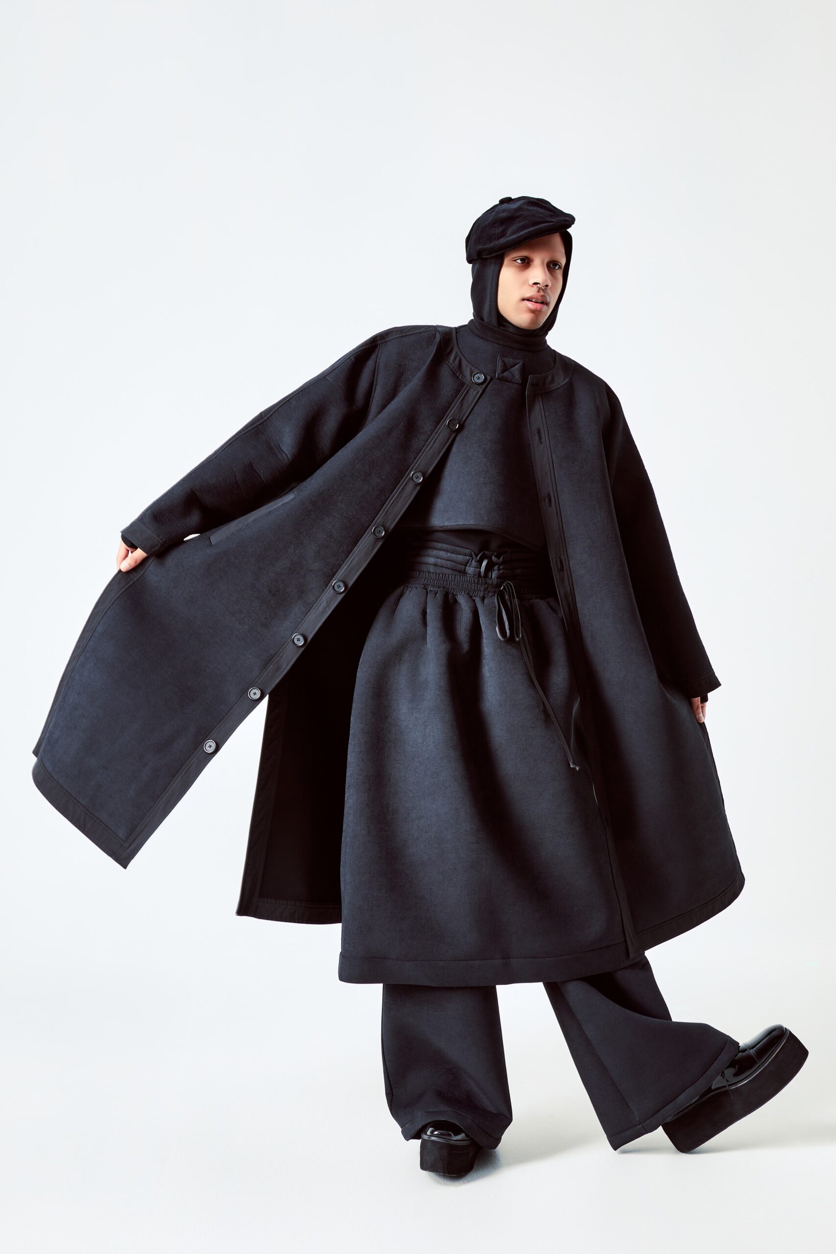 This ensemble features a relaxed black wool coat layered over matching pants, creating a cohesive silhouette. The long sleeves and collared design enhance the structured appearance, while the overall layering adds depth and movement to the look.