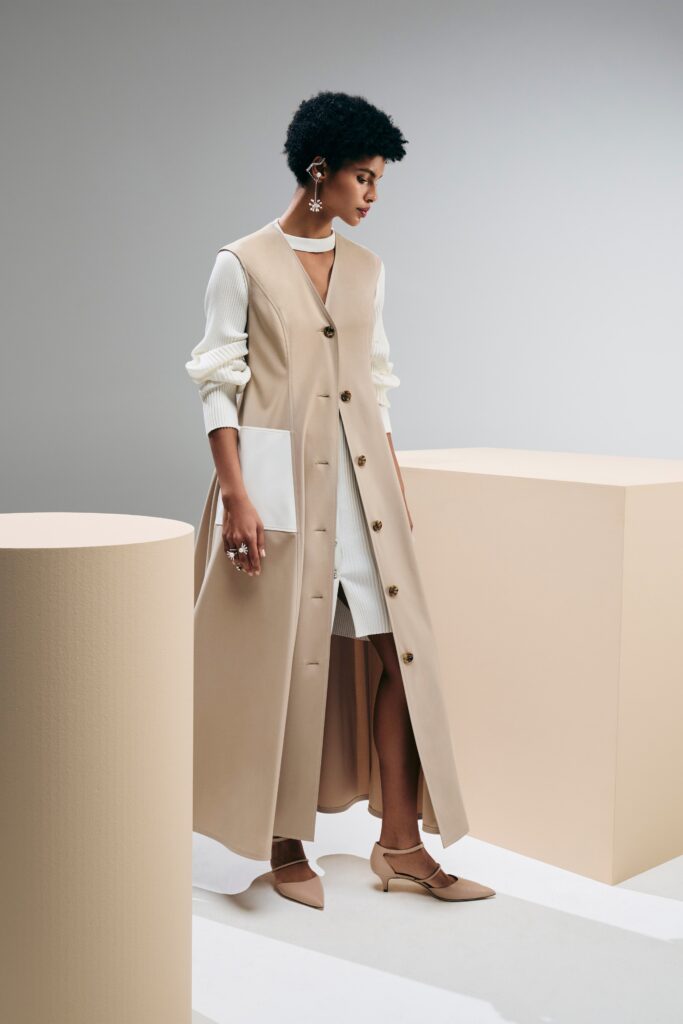 A fitted beige leather coat layered over a long-sleeve dress with button details.
