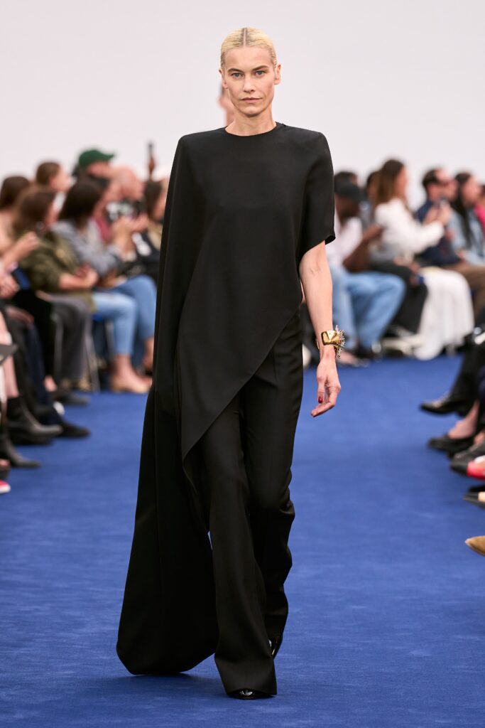 A fitted black silk cape paired with sleek black pants featuring an asymmetric design.