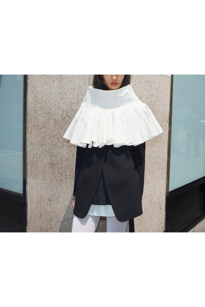 A relaxed black coat layered over a white ruffled blouse with long sleeves and a collared design.