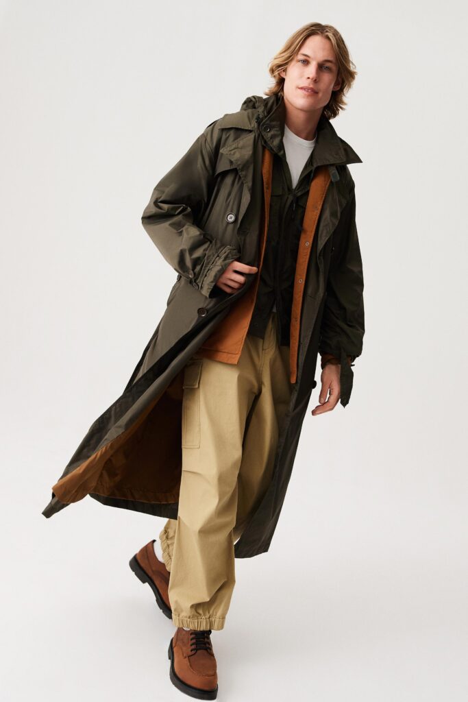 A relaxed green coat with long sleeves and a collared design paired with beige pants.