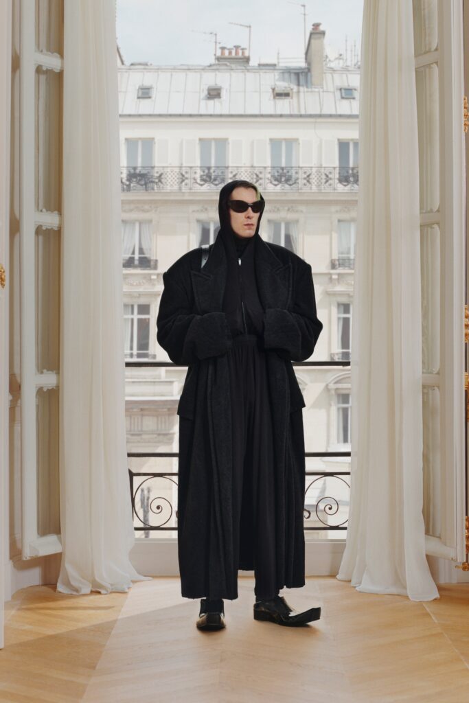 An oversized black wool coat with a hood and layered design details.
