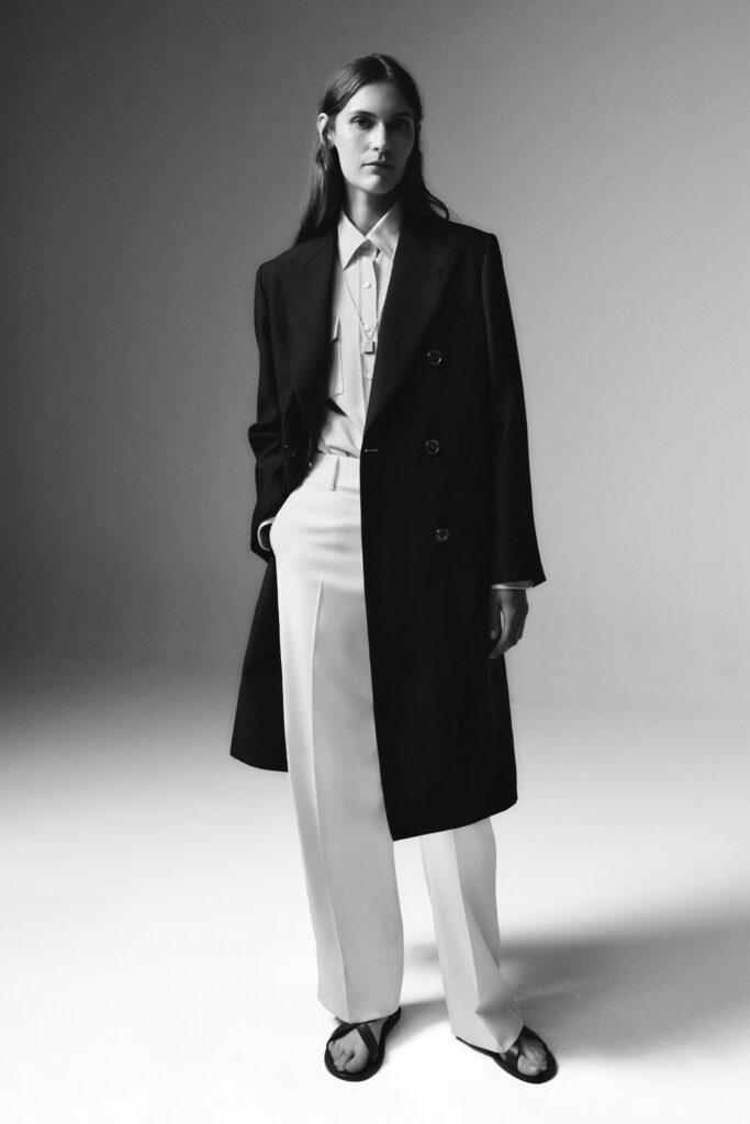 A fitted black coat paired with white straight-leg pants and a collared shirt.
