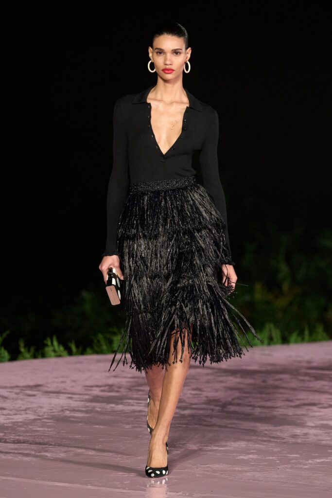 A fitted black silk dress with long sleeves, a V-neckline, and pleated detailing.
