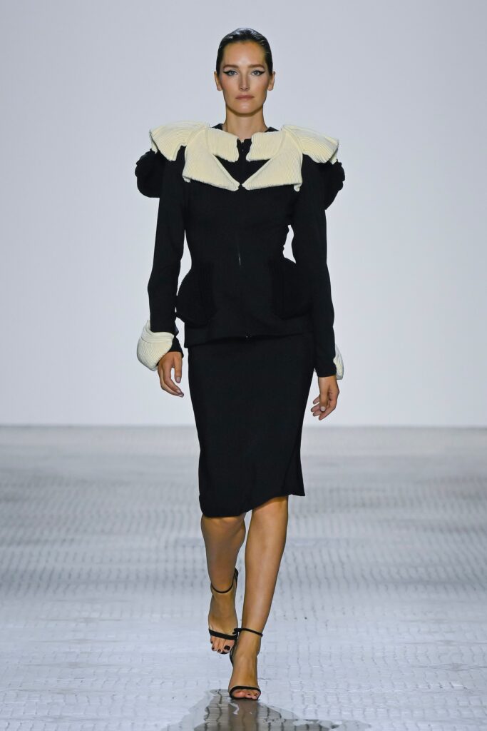 A fitted black dress featuring long sleeves, a V-neckline, and asymmetric design elements.