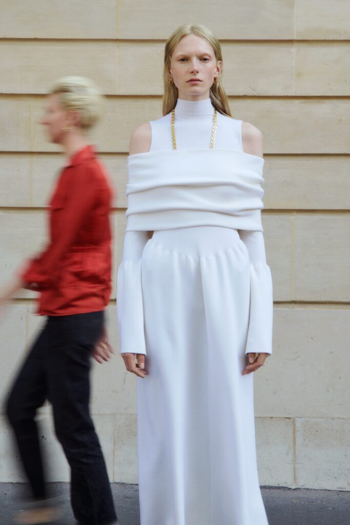 A fitted white long-sleeve dress with a high neckline and asymmetric design detail.