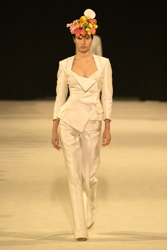 A fitted white silk blazer with long sleeves and a V-neck, paired with matching trousers.