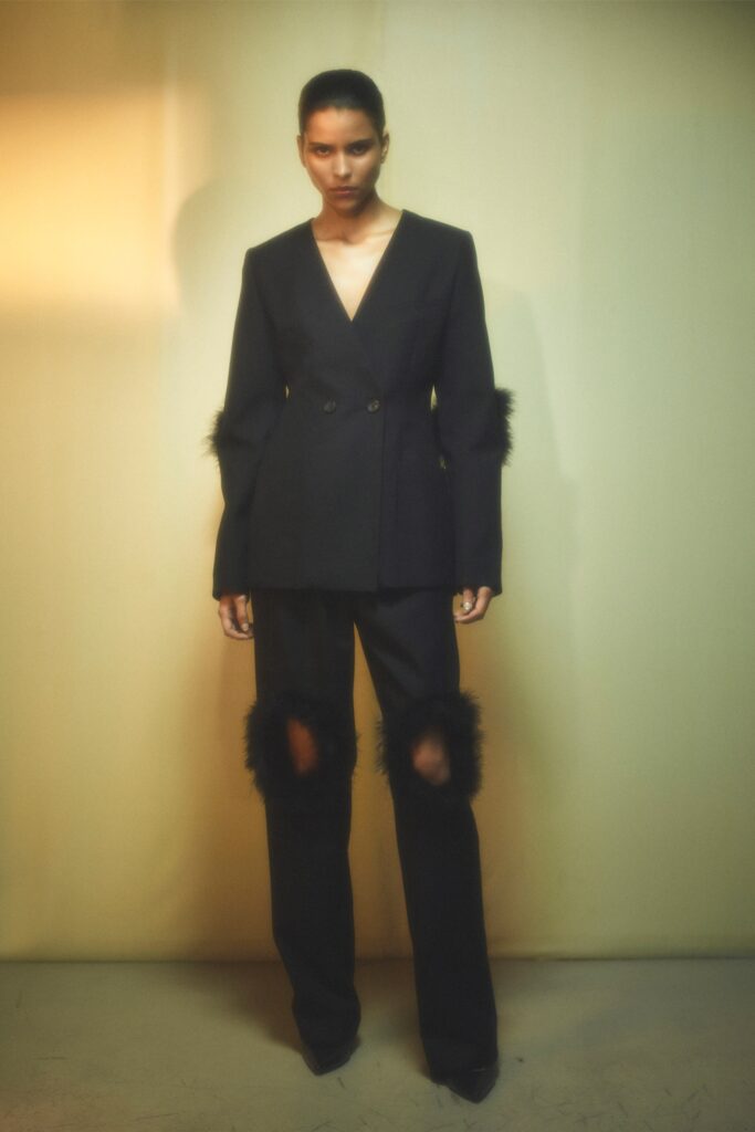 A fitted black blazer with long sleeves and fringed details paired with matching black pants.