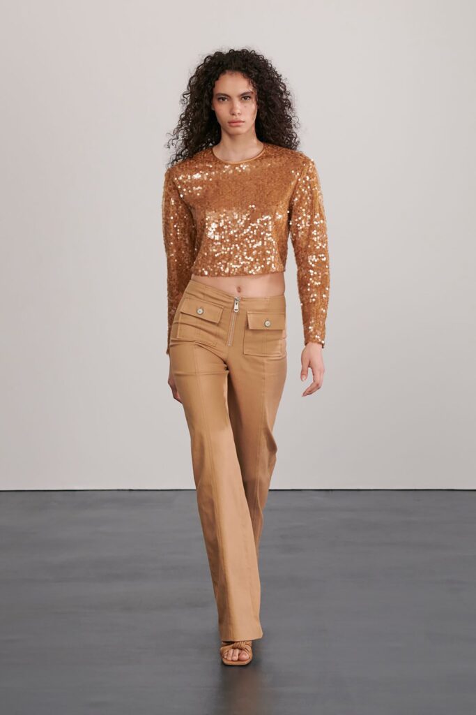 A fitted gold sequin cropped top paired with high-waisted beige pants featuring zipper details.