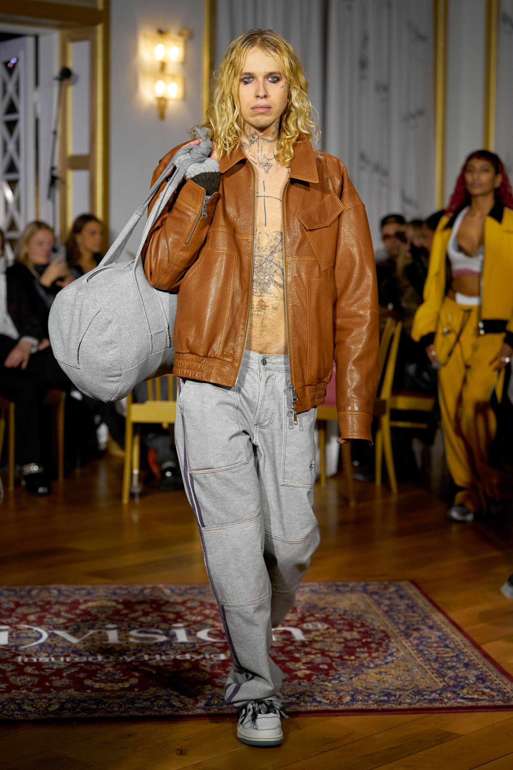 A relaxed brown leather jacket paired with gray cotton pants featuring a zippered detail.