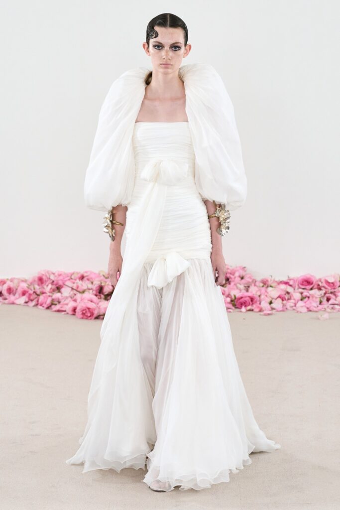 A fitted white silk gown with a high neckline and draped detailing.