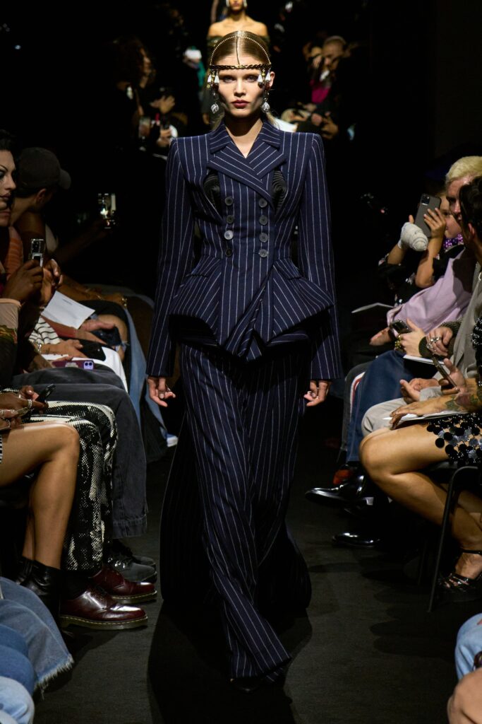 A fitted blue wool dress with long sleeves, a collared neckline, and an asymmetric pleated design.