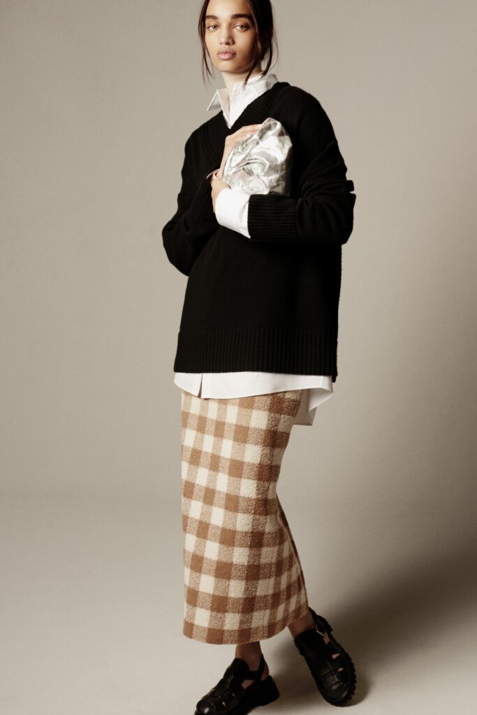 A relaxed black long-sleeve sweater paired with a tiered checked beige skirt.